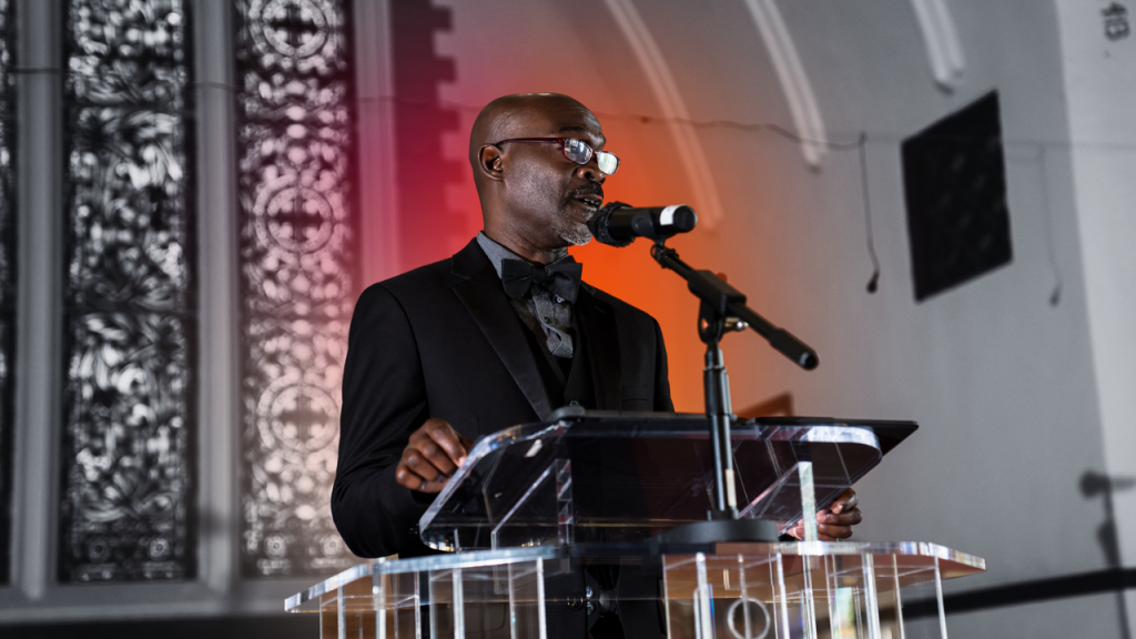 Image of a pastor preaching with red and orange colors behind him.